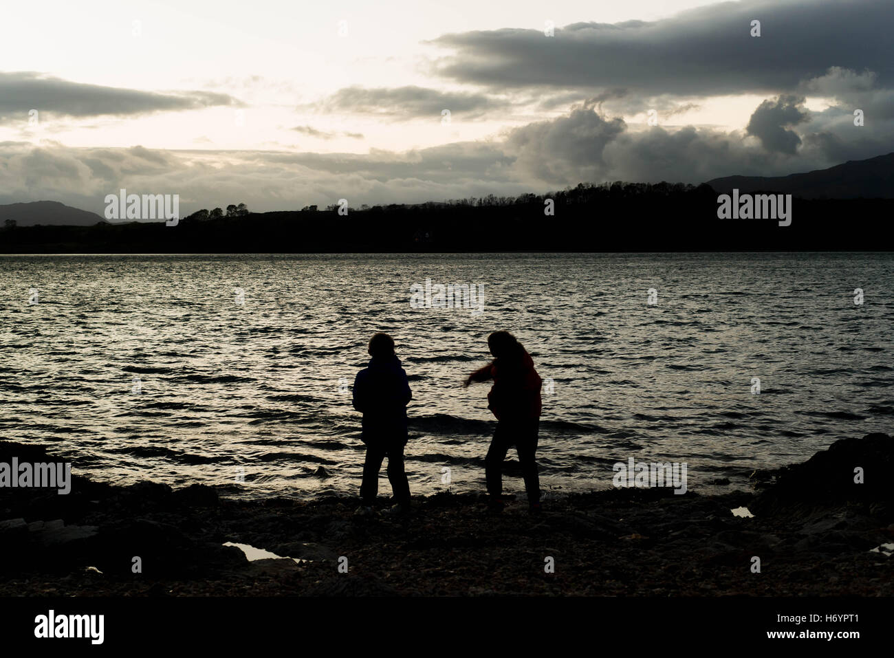 Silhouette von 2 jungen Steinewerfen ins Wasser, Port Appin Schottland im Herbst Stockfoto