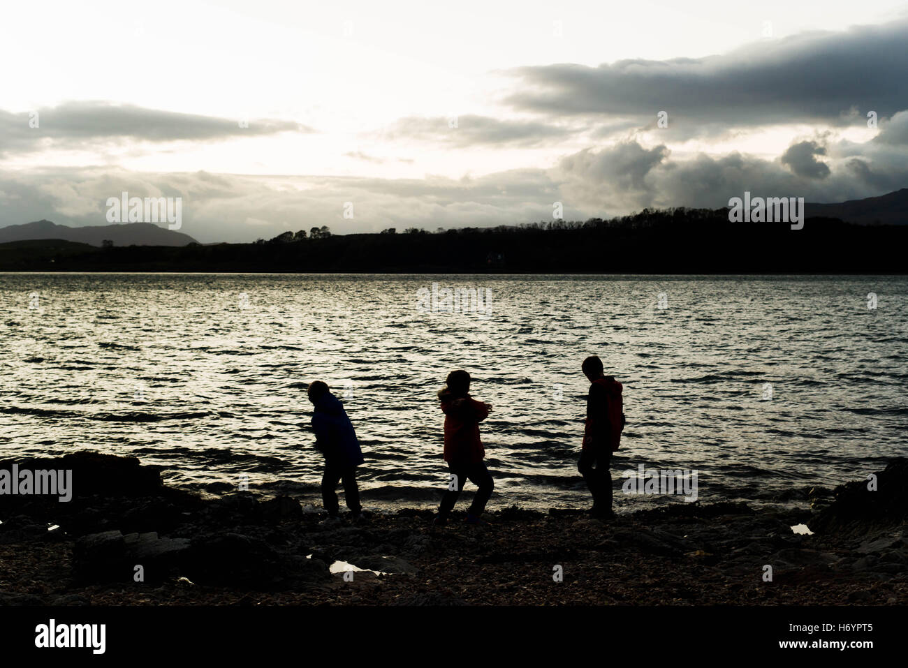 Silhouette von 3 jungen Steinewerfen ins Wasser, Port Appin Schottland im Herbst Stockfoto