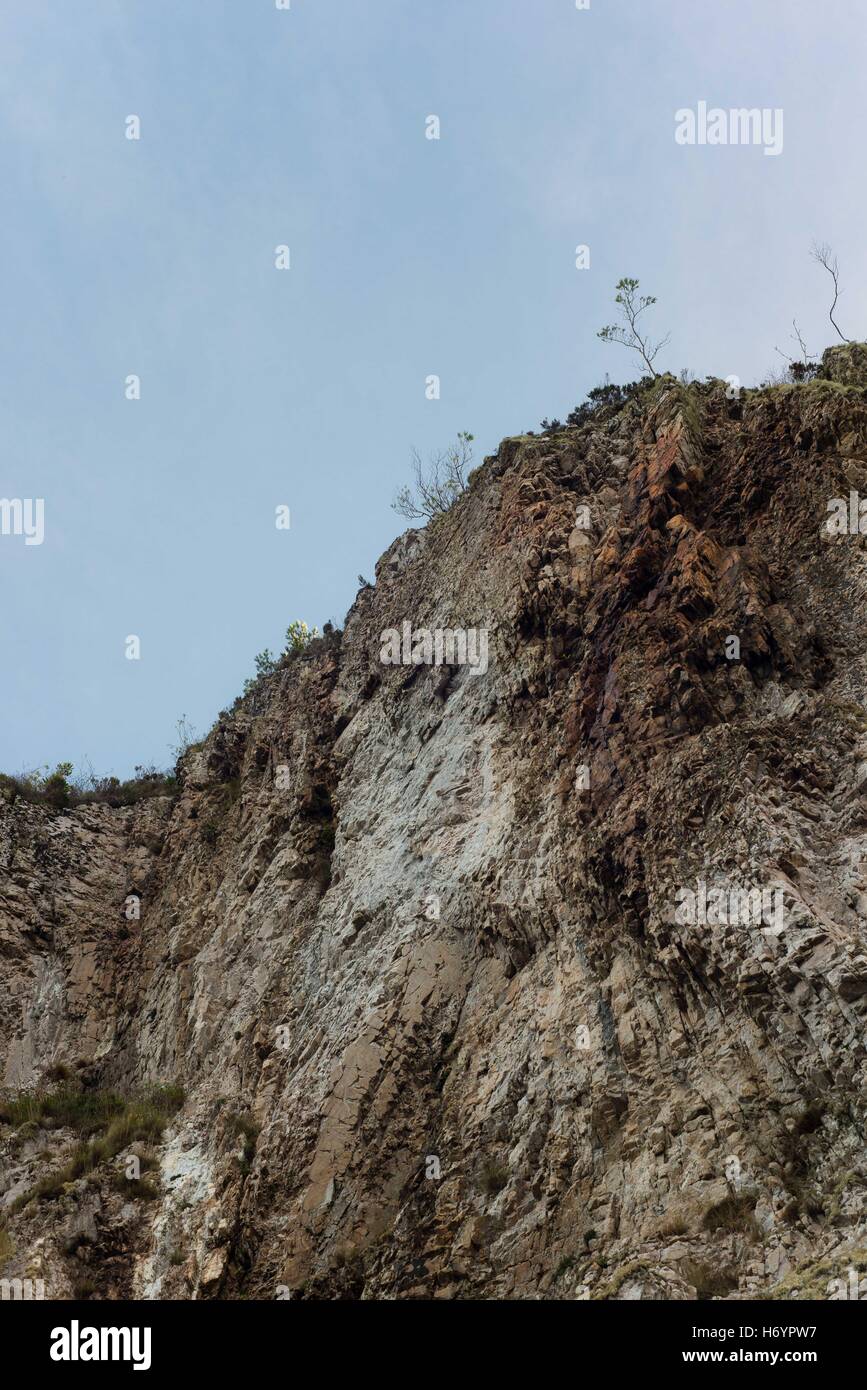 Felswand mit einigen Pflanzen an der Spitze mit einem Kontrast von blauem Himmel Stockfoto