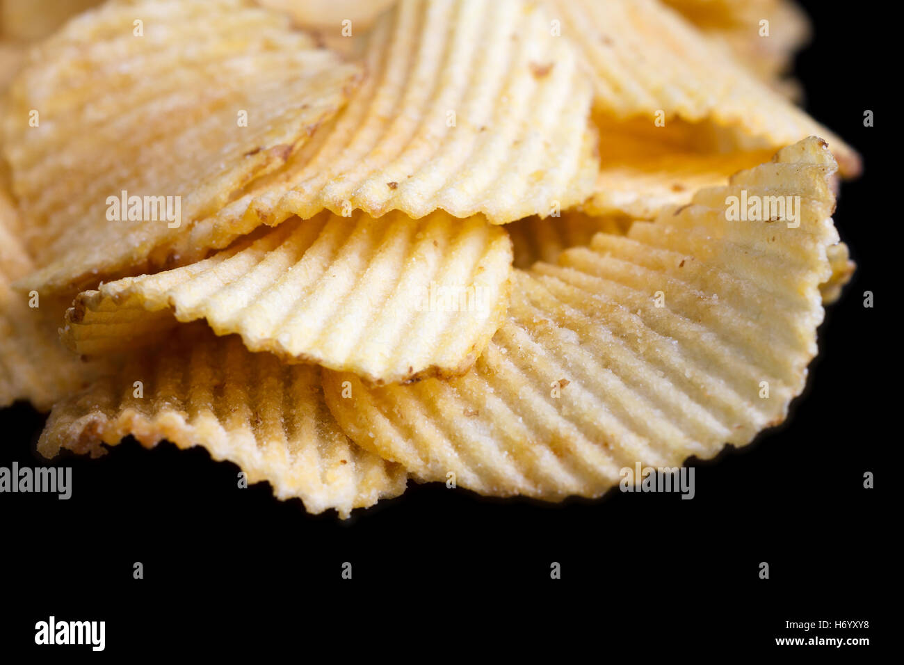 Geriffelte gebratene Kartoffelchips auf schwarz. Stockfoto