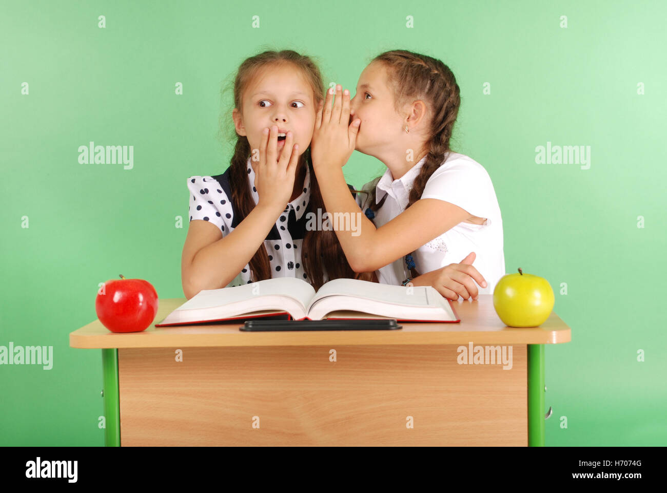 Zwei Schulmädchen Geheimnisse sitzen an einem Schreibtisch aus Buch isoliert auf grün Stockfoto