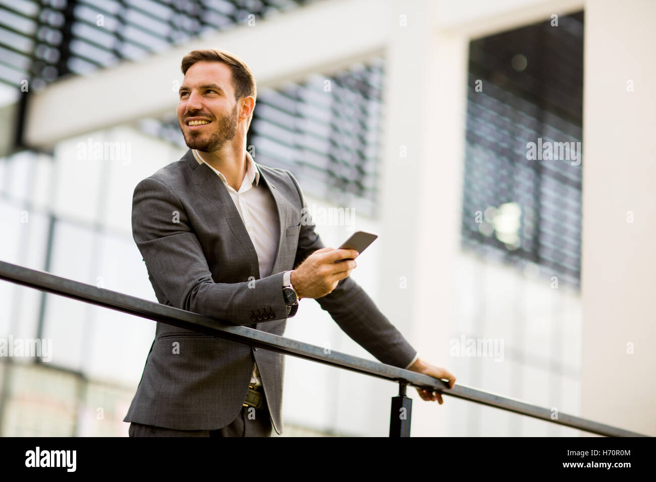 Erfolgreiche Jungunternehmer grauen Anzug trägt und hält sein Smartphone im stehen in der Nähe von modernen Büro oder Wolkenkratzern Stockfoto