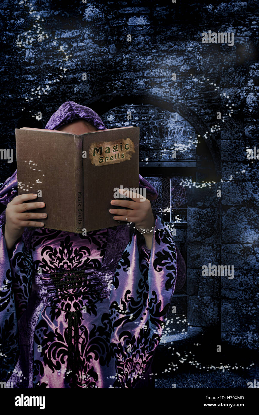 Hexe lesen aus einem Buch der Zaubersprüche in den Ruinen einer Abtei Stockfoto