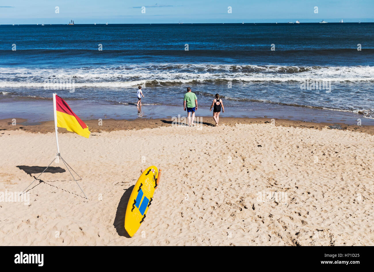 Eine Familie braucht, um das Meer an einem UK-Strand mit Bademeister das Surfbrett und Warnung Flagge im Vordergrund. Stockfoto
