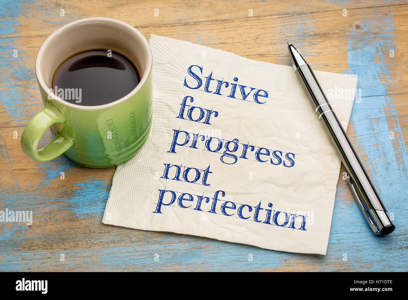 Streben Sie nach Fortschritt, nicht Perfektion - Handschrift auf einer Serviette mit einer Tasse Espressokaffee Stockfoto
