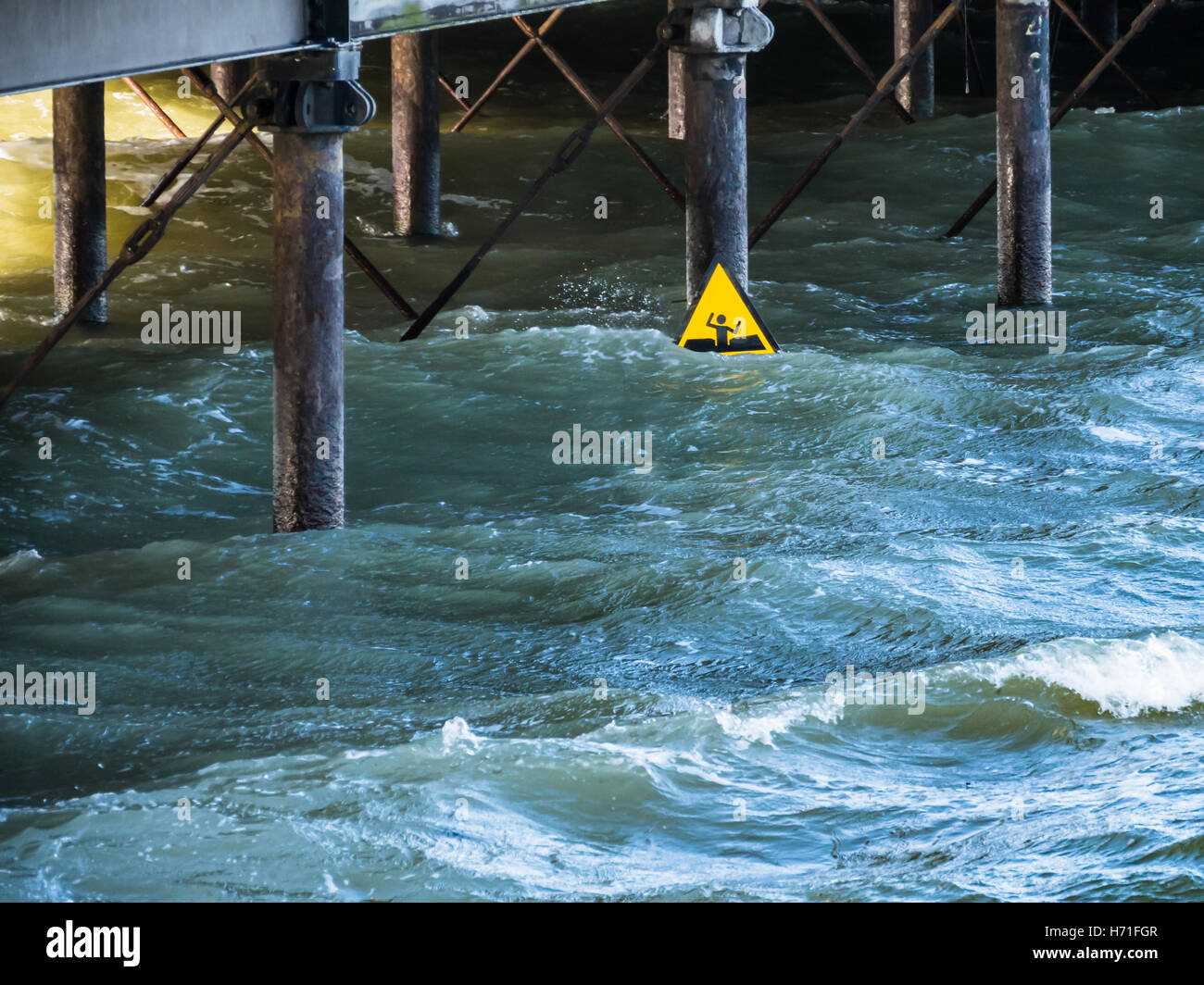 Ein gelbes Warnschild für weichen Schlamm sieht aus wie ein Mann winken für Hilfe vor dem Ertrinken unter einem Pier in tiefen kalten Wasser auf einem w suchen Stockfoto
