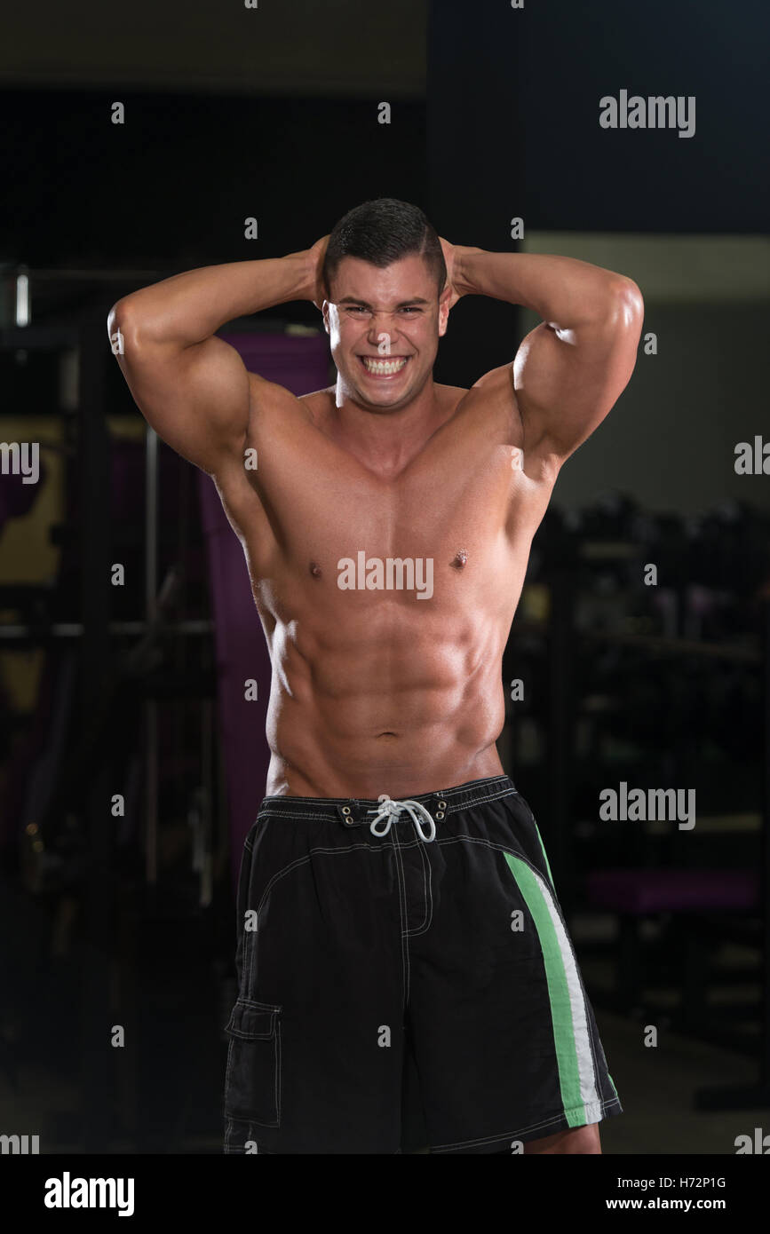 Junger Mann stehen stark In der Turnhalle und biegen Muskeln - muskulöse athletische Bodybuilder Fitness Model posiert mit Abs nach Stockfoto
