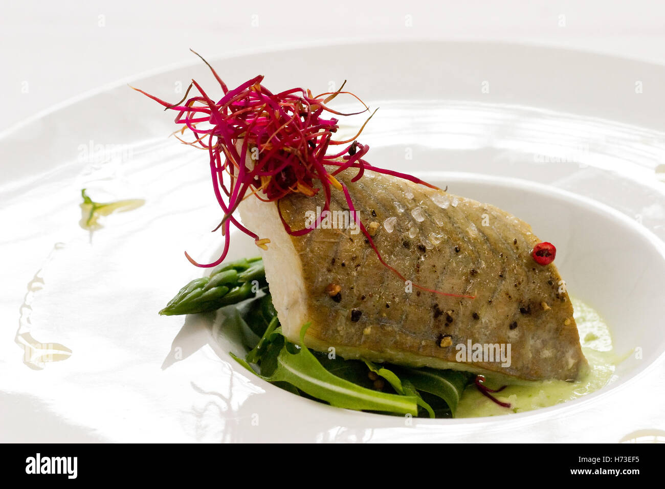 Gegrillter weißer Fisch mit Haut auf Spargel und garniert mit Safran Stockfoto