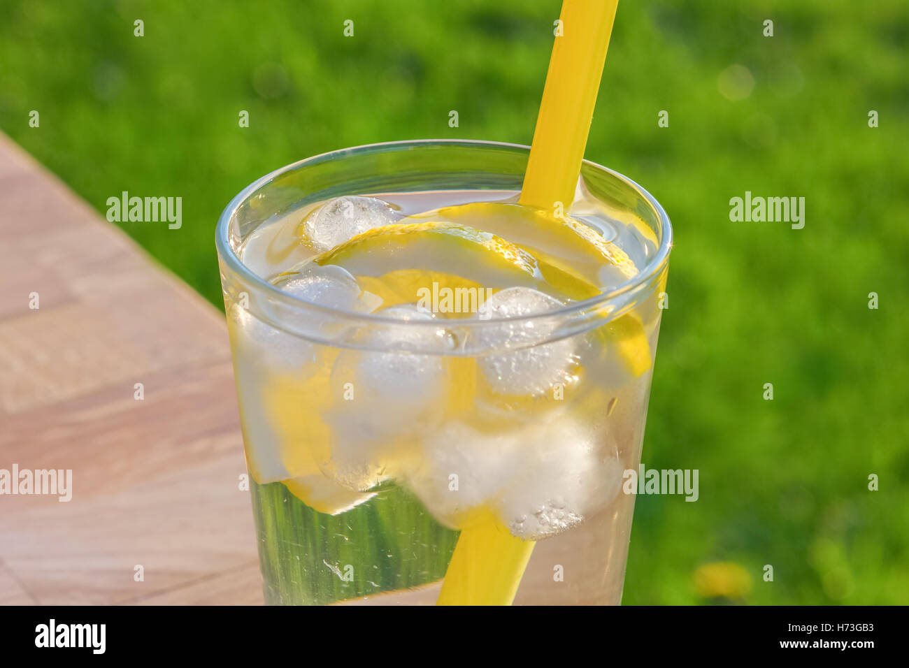 Einfaches Glas Eiswasser mit Zitronenscheiben und Stroh auf einem Tisch. Im Freien mit einem Fokus Rasen Hintergrund in weichen Su genommen Stockfoto
