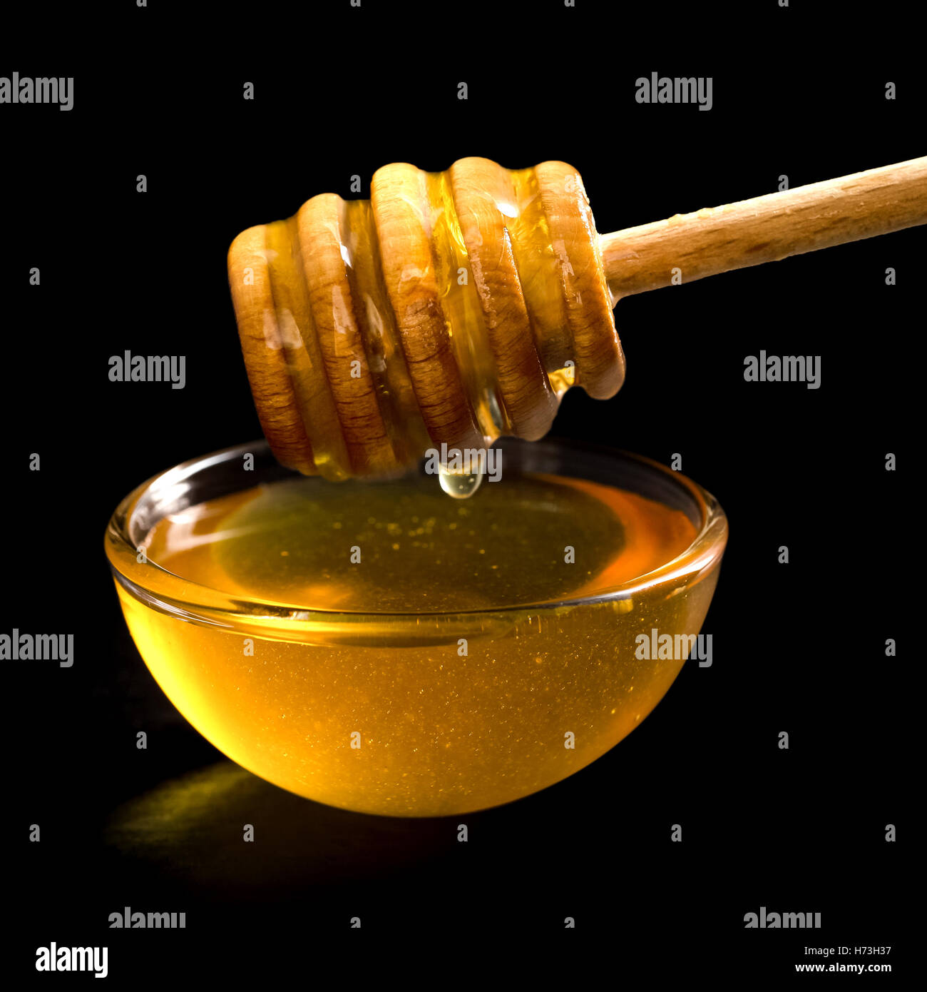 Hölzerne Honig Schöpflöffel über Glasschale mit Honig gefüllt. Schwarzer Hintergrund. Stockfoto