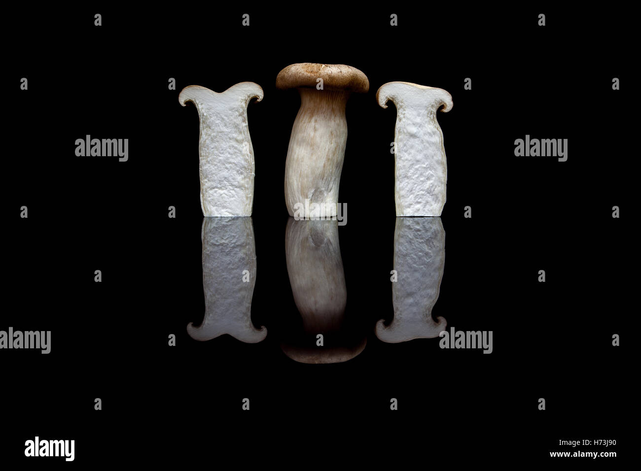 Drei aufrechte König Austernpilze, einem ganzen und zwei halbiert auf schwarzen reflektierenden Hintergrund isoliert Stockfoto