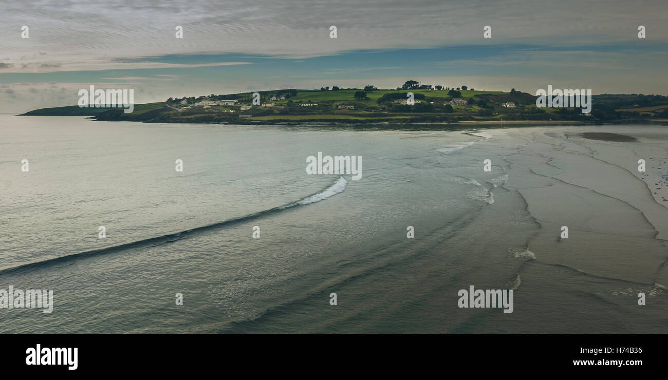 Sanfte Wellen brechen sich am Strand beim Sonnenuntergang auf einer wunderschönen Insel wie Siedlung im Hintergrund. Irland, 2016 Stockfoto