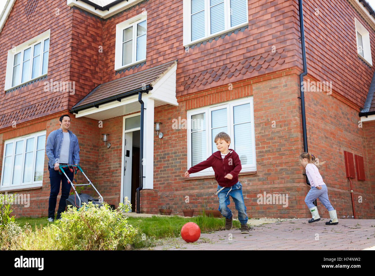 Kinder spielen im Garten als Vater mäht Rasen vor Haus Stockfoto