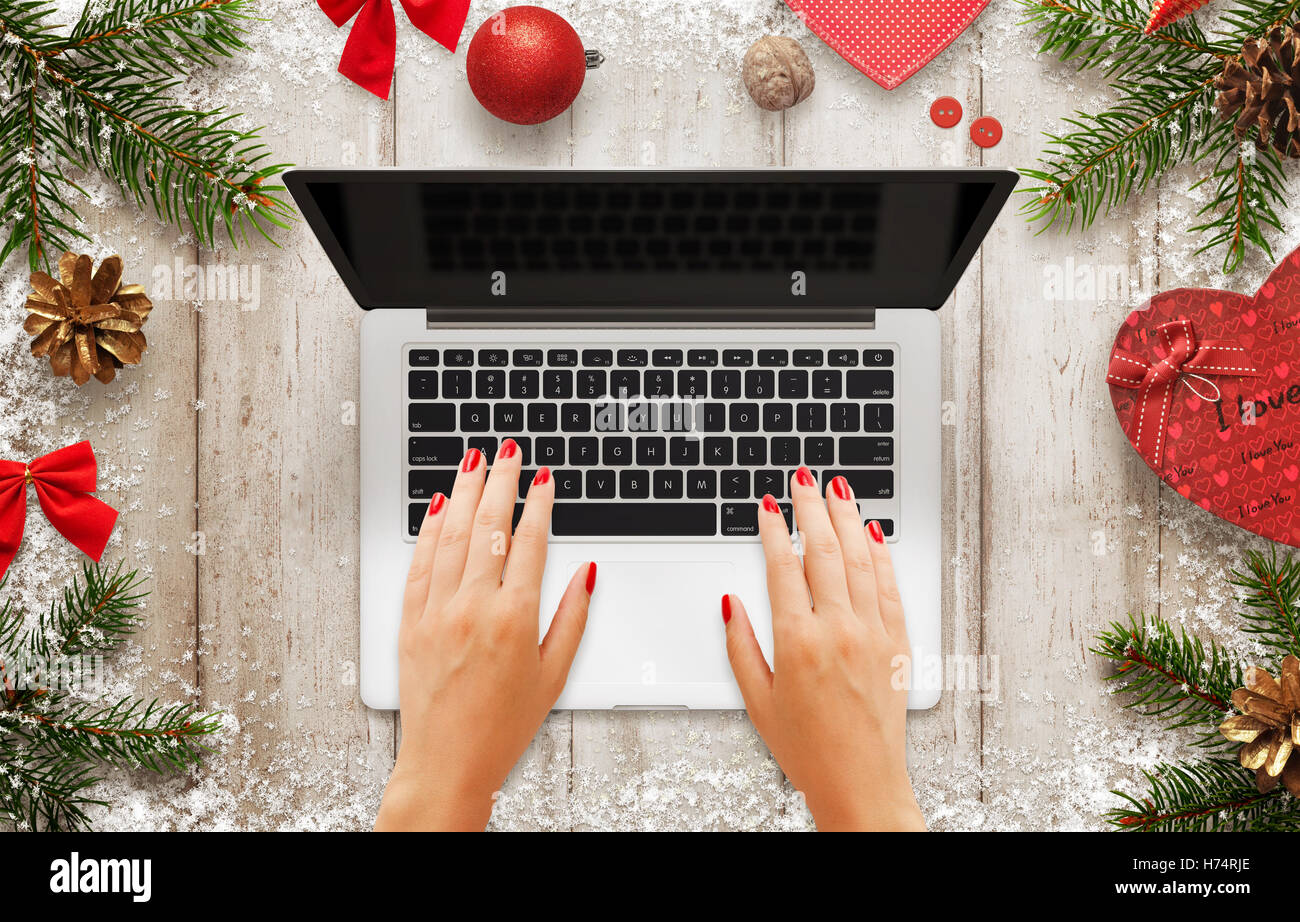 Frau Arbeit am Laptop. Weihnachtsszene mit Dekorationen, Baum und Geschenk. Leerer Bildschirm für Mock-up. Draufsicht der Tabelle. Stockfoto