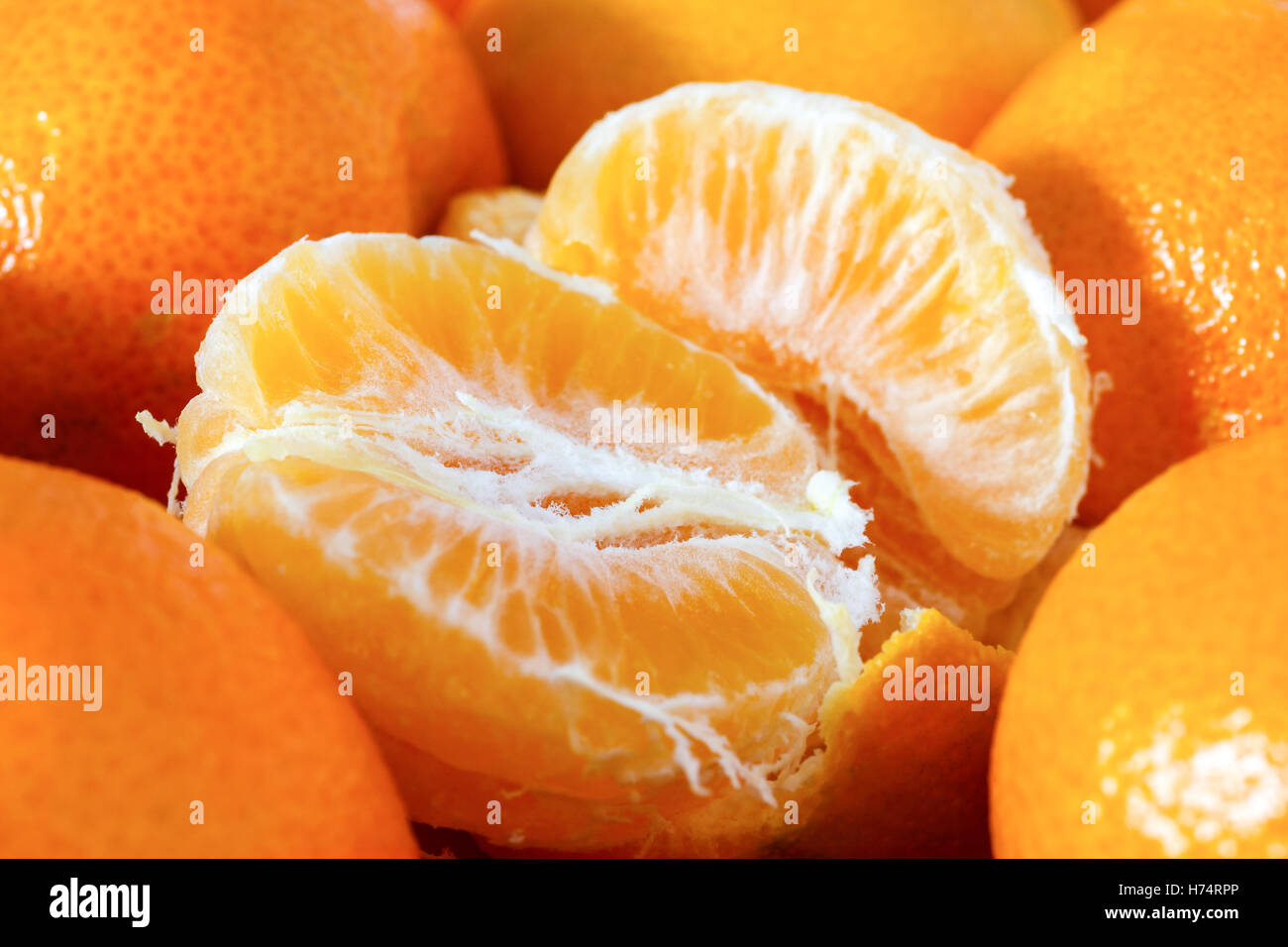 Halb geschälte Mandarine umgeben von ungeschälten Mandarinen Stockfoto