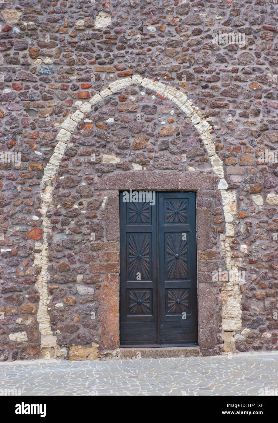 Die moderne Tür befindet sich in dem alten Bogen der mittelalterlichen Kathedrale in Castelsardo, Sardinien, Italien. Stockfoto