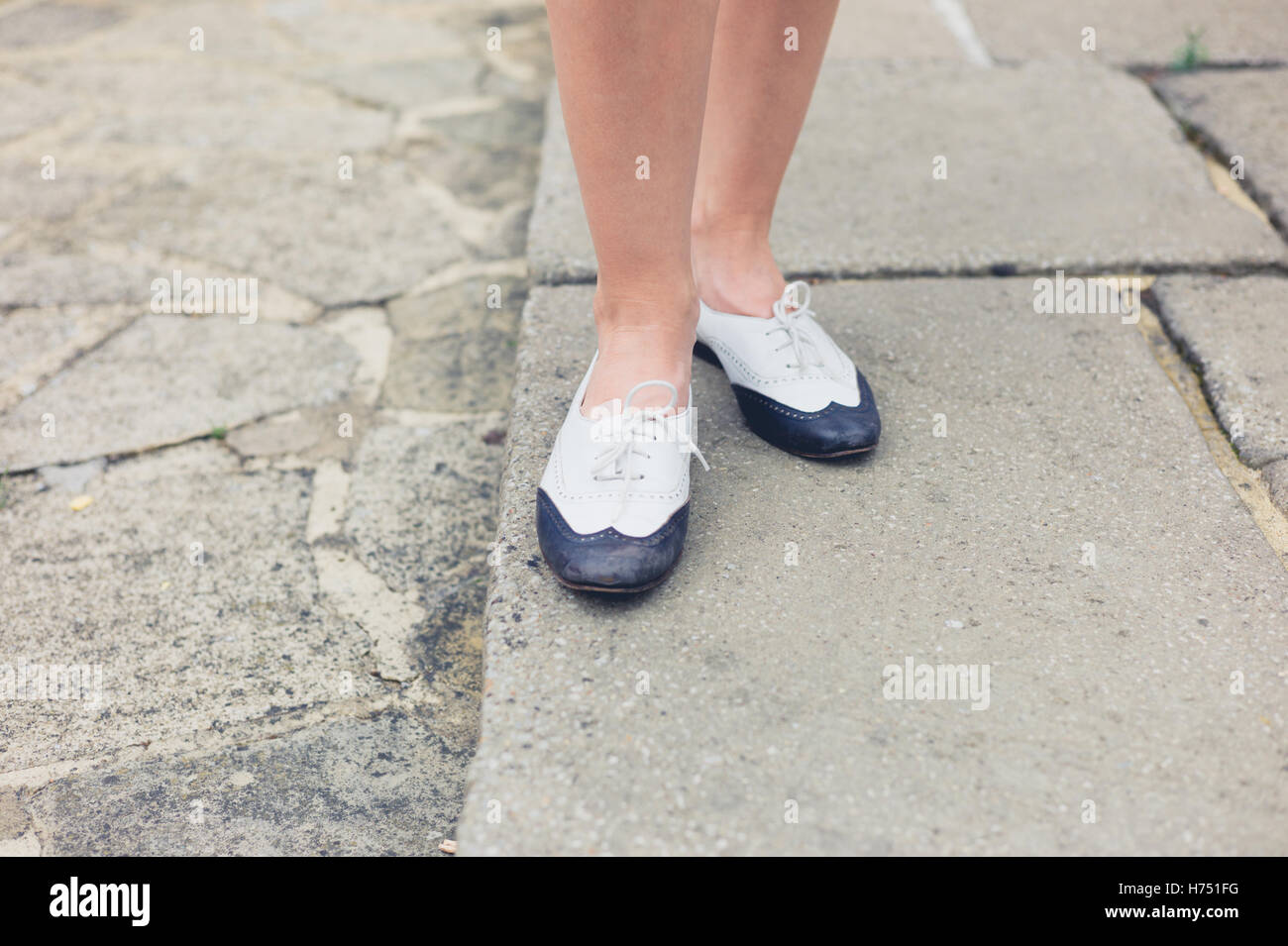 Die Füße einer jungen Frau, die elegante zweifarbige Schuhe tragen, da sie auf einer Veranda steht Stockfoto
