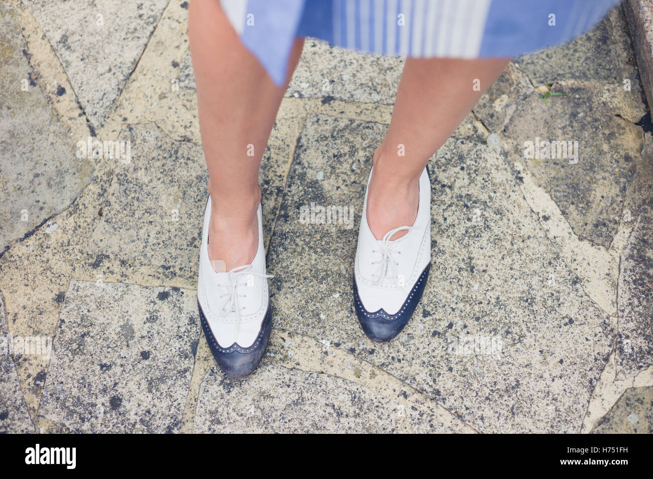 Die Füße einer jungen Frau, die elegante zweifarbige Schuhe tragen, da sie auf einer Veranda steht Stockfoto