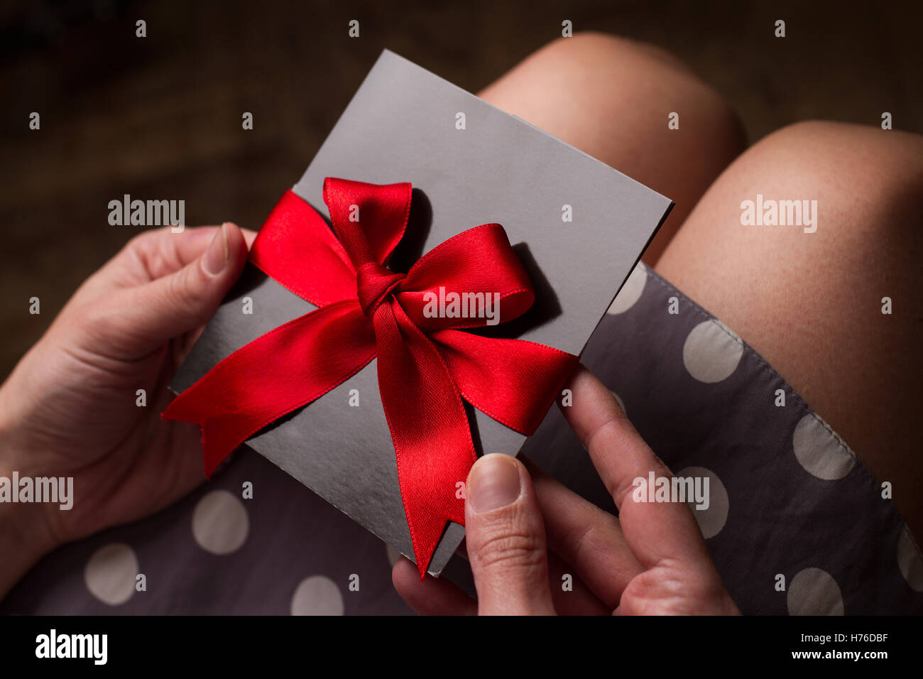 Nahaufnahme von den Händen einer Frau mit Polka Kleid hielt eine schwarze Karte mit rotem Band über Knie Stockfoto
