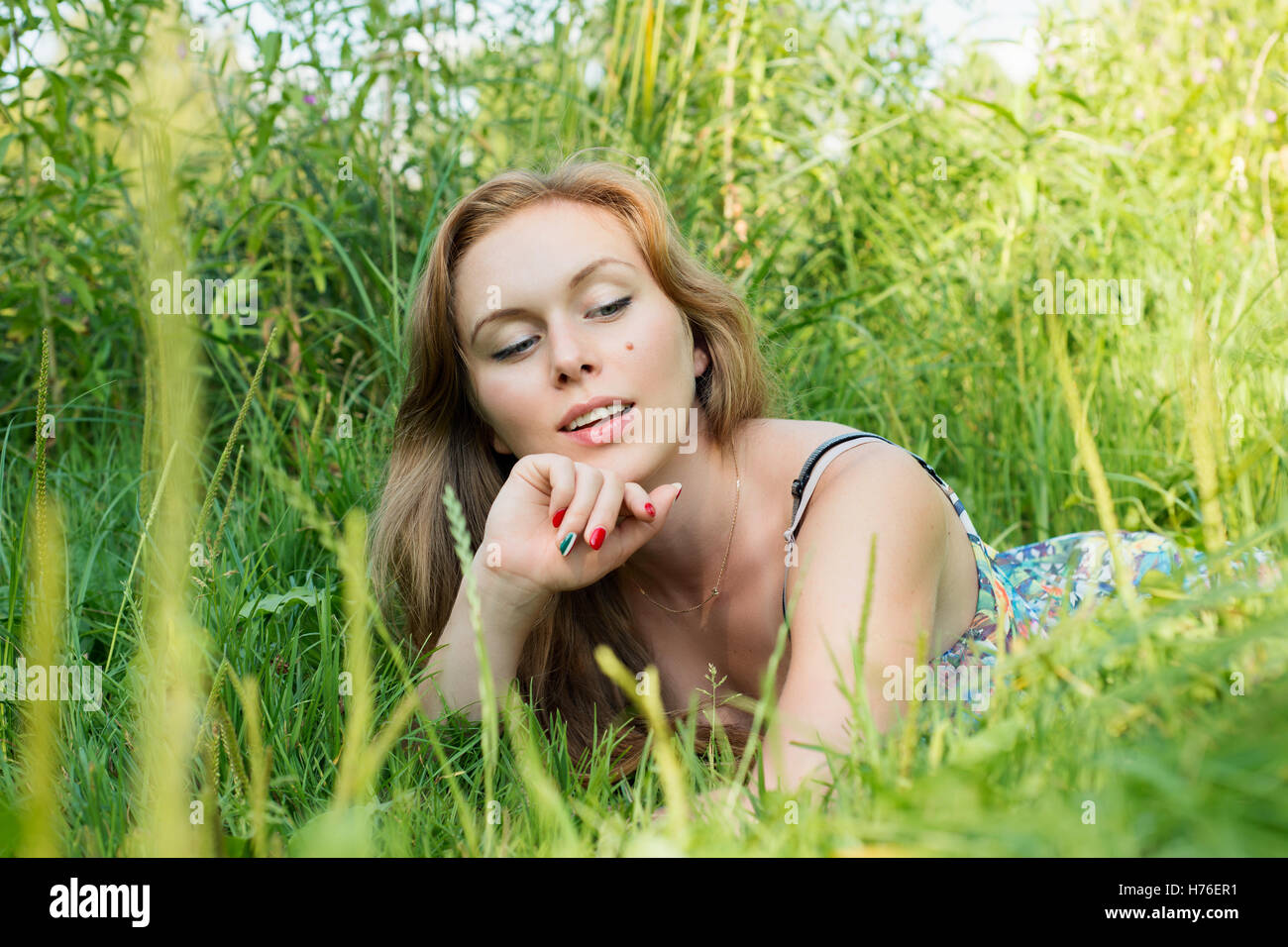 Junge Frau mit langen Haaren, die im Sommer auf der Wiese liegend Stockfoto