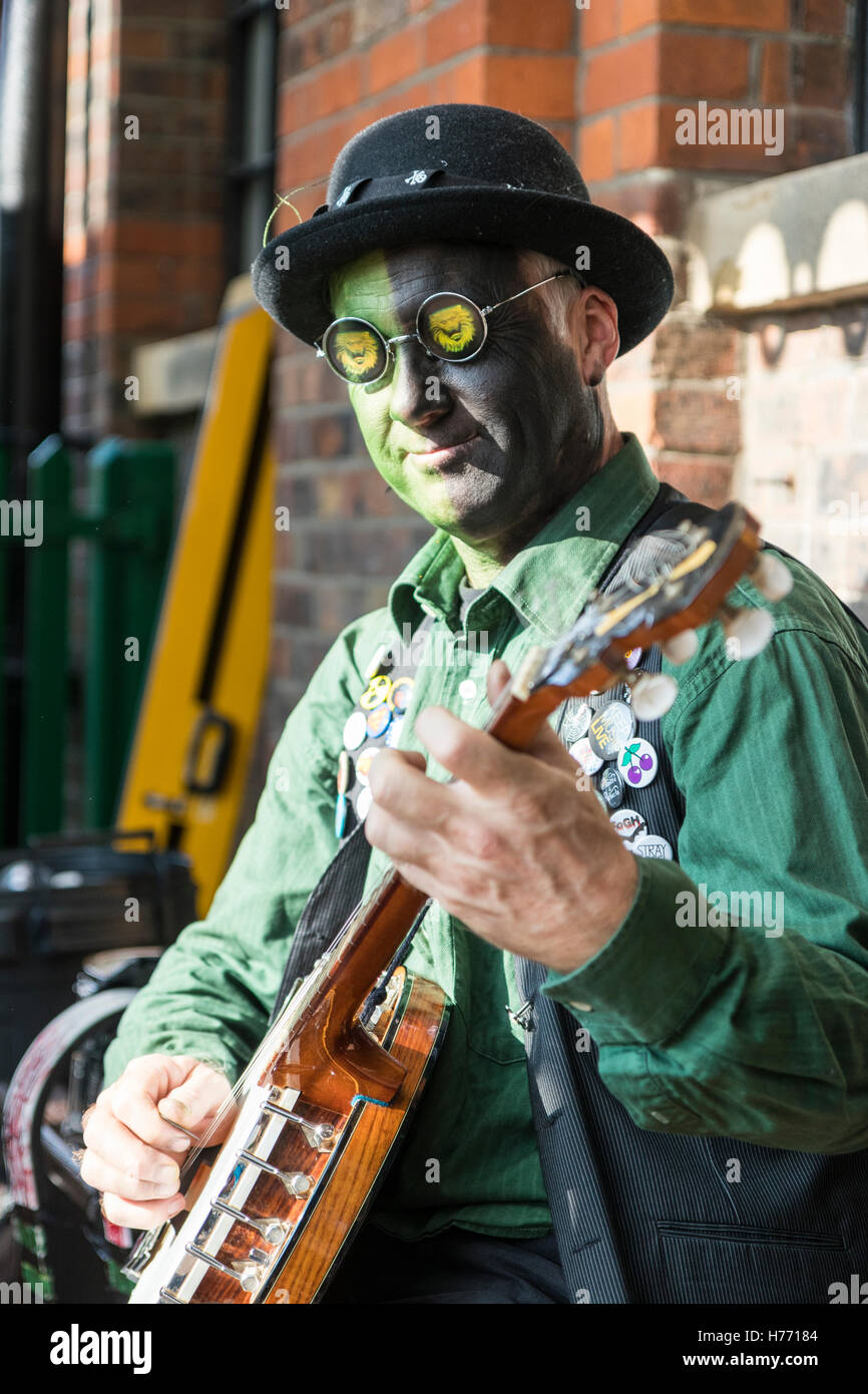 Besen Ziegel und Bowlers Grenze Morris Mann spielen Tenor Banjo. Gesicht malen Schwarz und Grün, und trägt schwarze Sonnenbrille. Close-up. Stockfoto