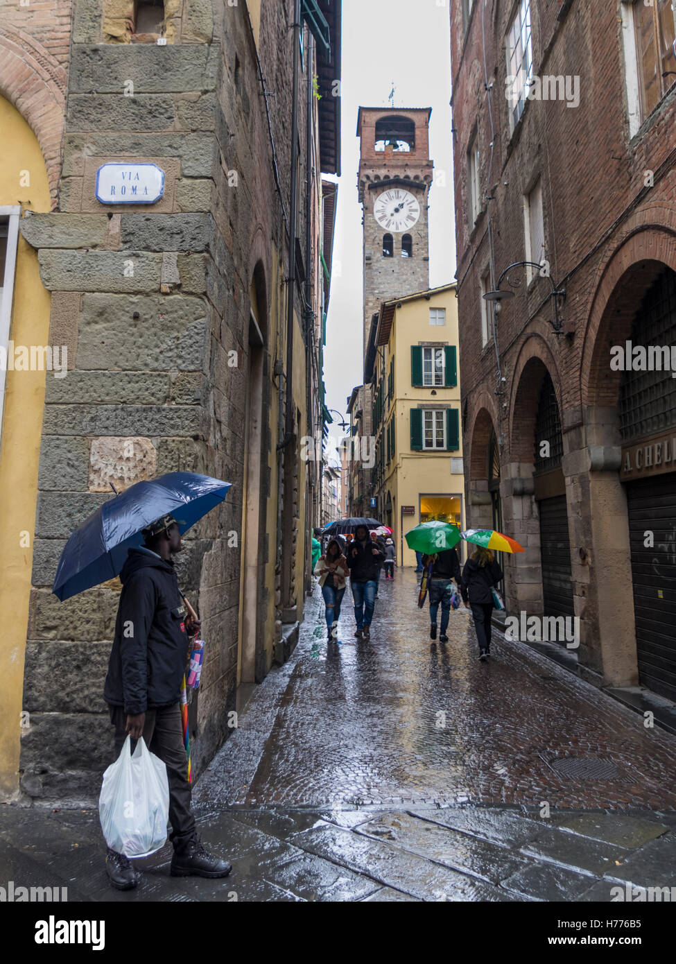Menschen mit Regenschirmen in einer engen Straße in der Altstadt von Lucca, Toskana, Italien, an einem regnerischen Tag. Stockfoto