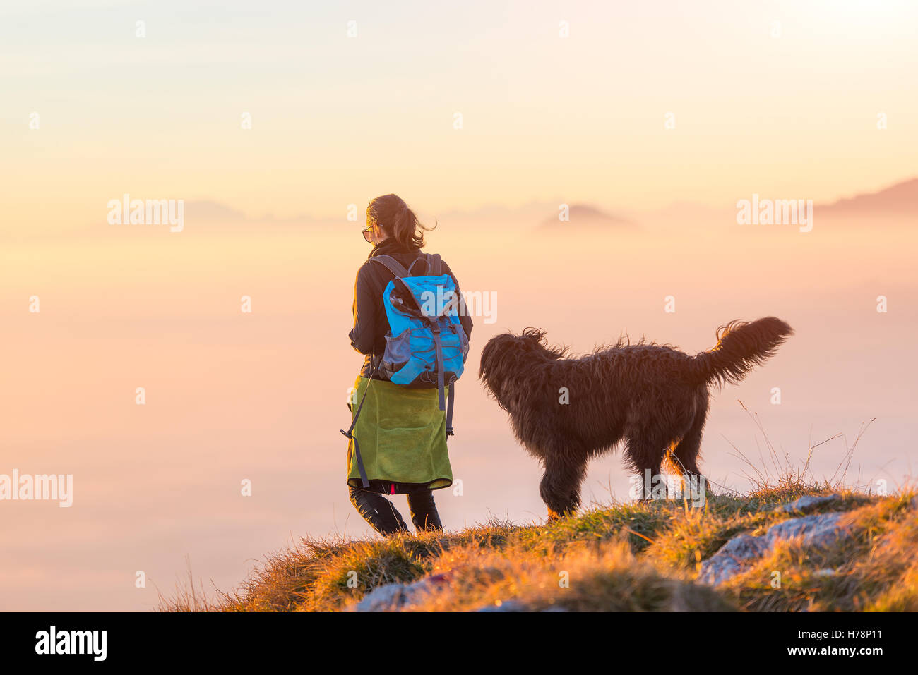 Frau mit ihrem schwarzen Schäferhund zu Fuß auf einem Berg über dem Nebelmeer Stockfoto