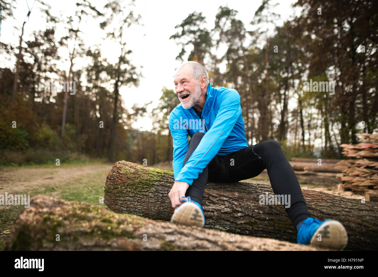 Senior Läufer sitzt auf hölzernen anmeldet, man ruht, stretching. Stockfoto