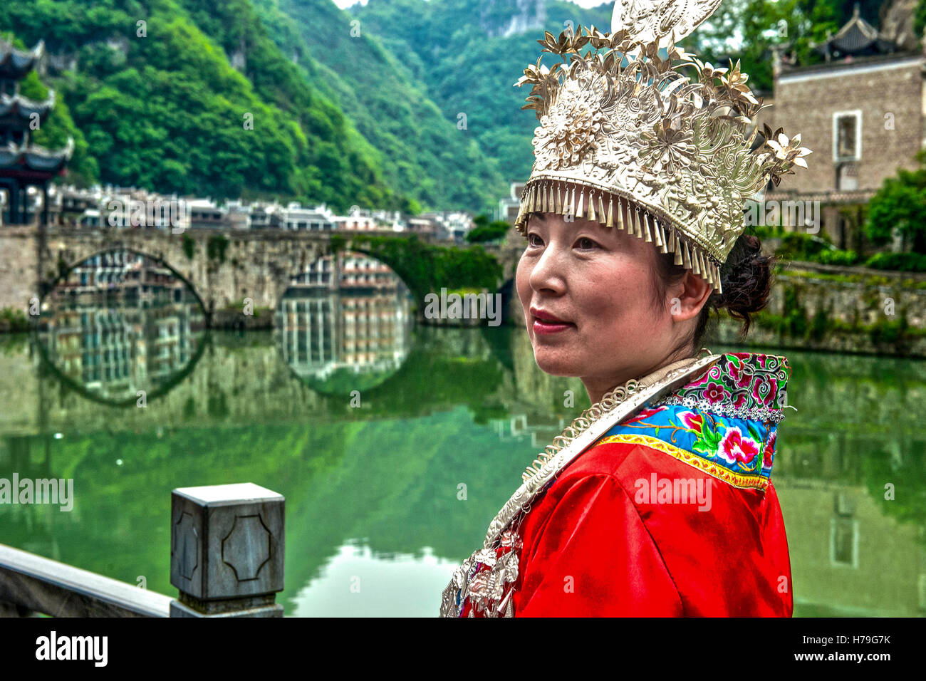 Frau gekleidet in typische Miao-Kostüm und Brücke über Wuyang Fluss im Hintergrund, in Zhenyuan, Guizhou (China) Stockfoto