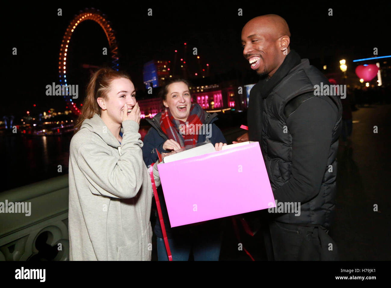 NUR zur redaktionellen Nutzung (von links nach rechts) Rebecca Knox und Alison McGregor erhalten eine frühe Weihnachtsgeschenk von Geschenk-Geber Kiell Smith-Bynoe auf Westminster Bridge in London, als eine Projektion auf London County Hall zeigt Online-Händler Very.co.uk Weihnachten Werbung. Stockfoto