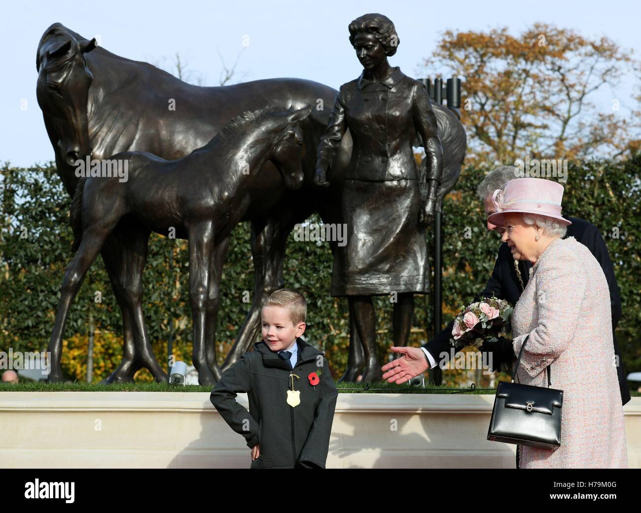 Königin Elizabeth II erhält Blumen von Thomas Cotton, acht aus Bury St Edmunds in Newmarket Racecourse, nachdem sie eine Statue von sich selbst mit einem Fohlen und eine Stute als Geschenk im Jahr von ihrem 90. Geburtstag, bei einem Besuch in der Stadt oft enthüllt bezeichnete als Hauptquartier der britischen Rennsport. Stockfoto