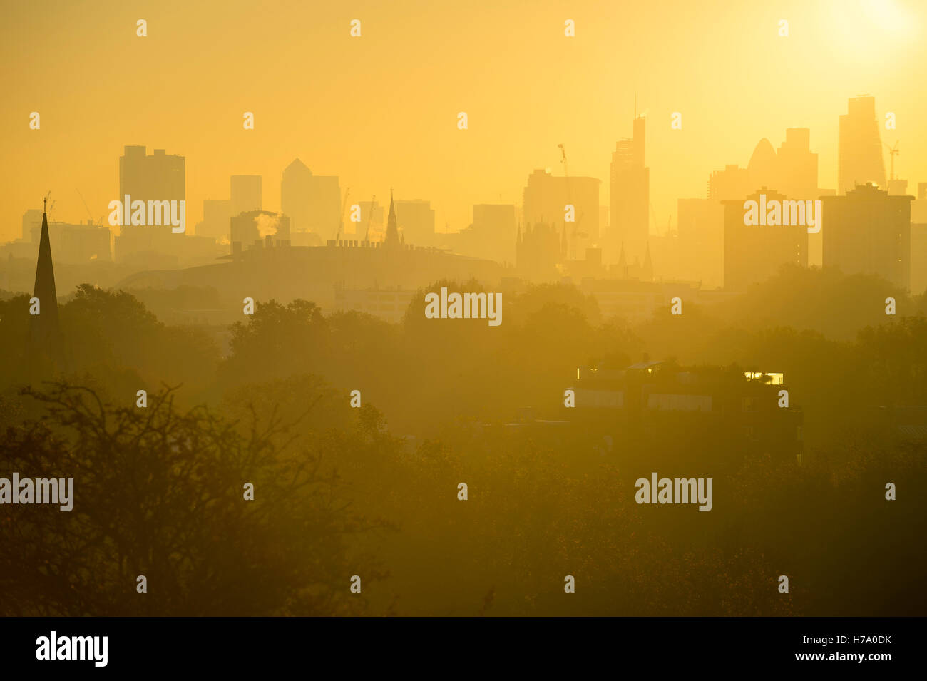 Golden Sunrise Skyline von London, England mit modernen Wolkenkratzern, spähen über dem nebligen Parklandschaft Bäume Stockfoto
