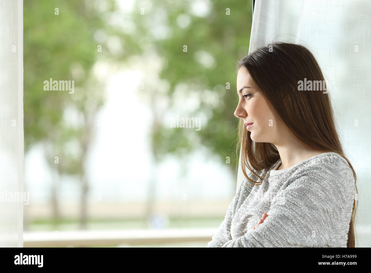 Profilbildnis einer Sehnsucht Frau im freien Blick durch ein Fenster zu Hause oder im Hotelzimmer mit einem grünen Hintergrund Stockfoto