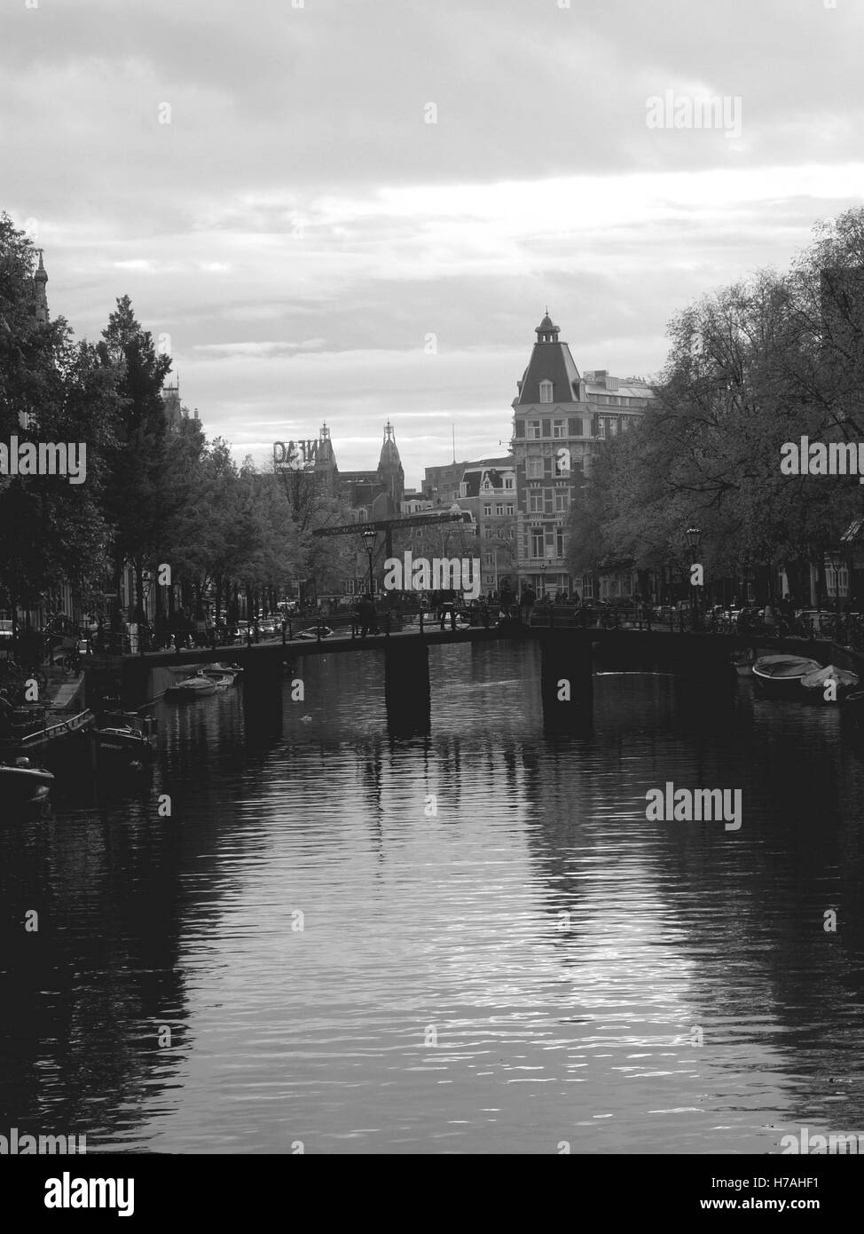 Schwarz / weiß-Kanal in Amsterdam im Herbst. Zentrale Sicht auf einen Wasserkanal mit einer Brücke und Türme in der Ferne. Stockfoto