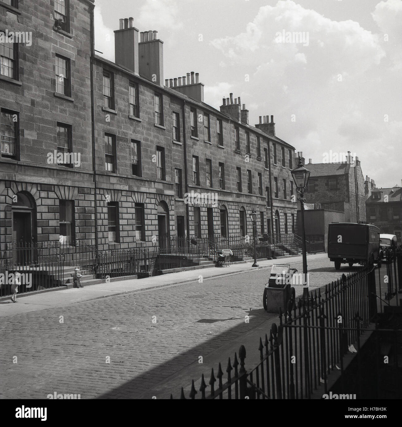 1950er-Jahren, historische, A gepflasterten Straße des späten georgischen terrassierten Gehäuse mit Kellern unter Edinburgh Schloß, Edinburgh, Schottland. Beachten Sie die leeren Kinderwagen auf dem Bürgersteig. Stockfoto