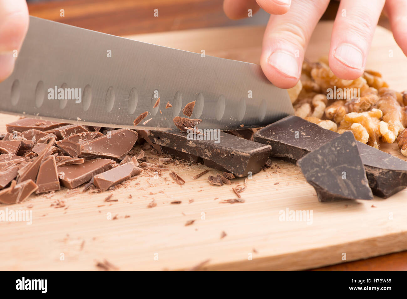 Chef hacken Schokolade mit Messer auf Schneidebrett. Dessert-Zubereitung in der Küche mit heller und dunkler Schokolade. Stockfoto
