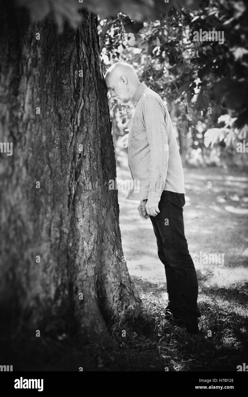Porträt des alten Mannes an einen Baum gelehnt. Konzept des Alters und Natur. Ruhestand und Frustration. Stockfoto