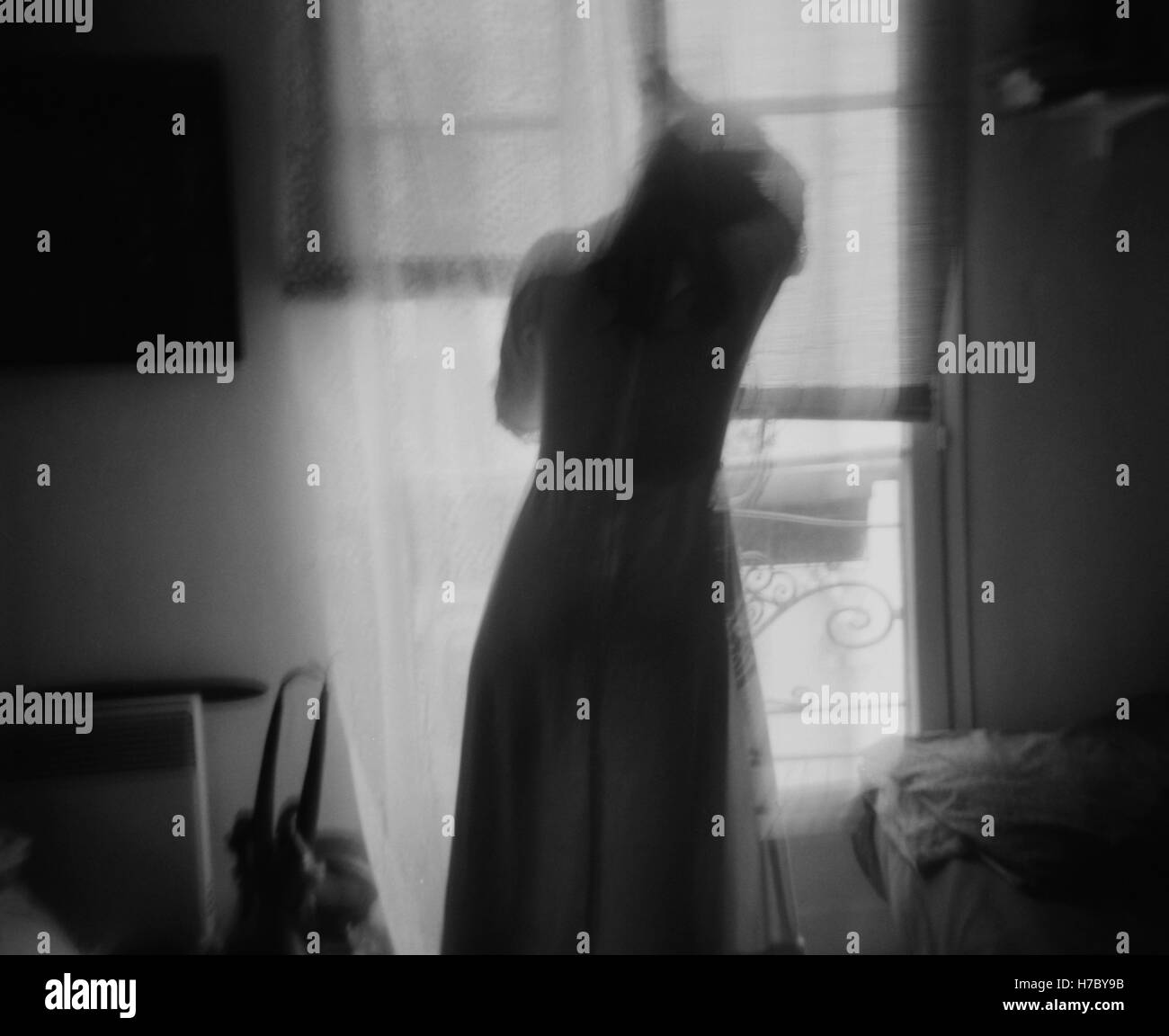 Das Mädchen im Fenster. Ein Mädchen in der Nacht Kleid Stellung in einem französischen Fenster. Stockfoto