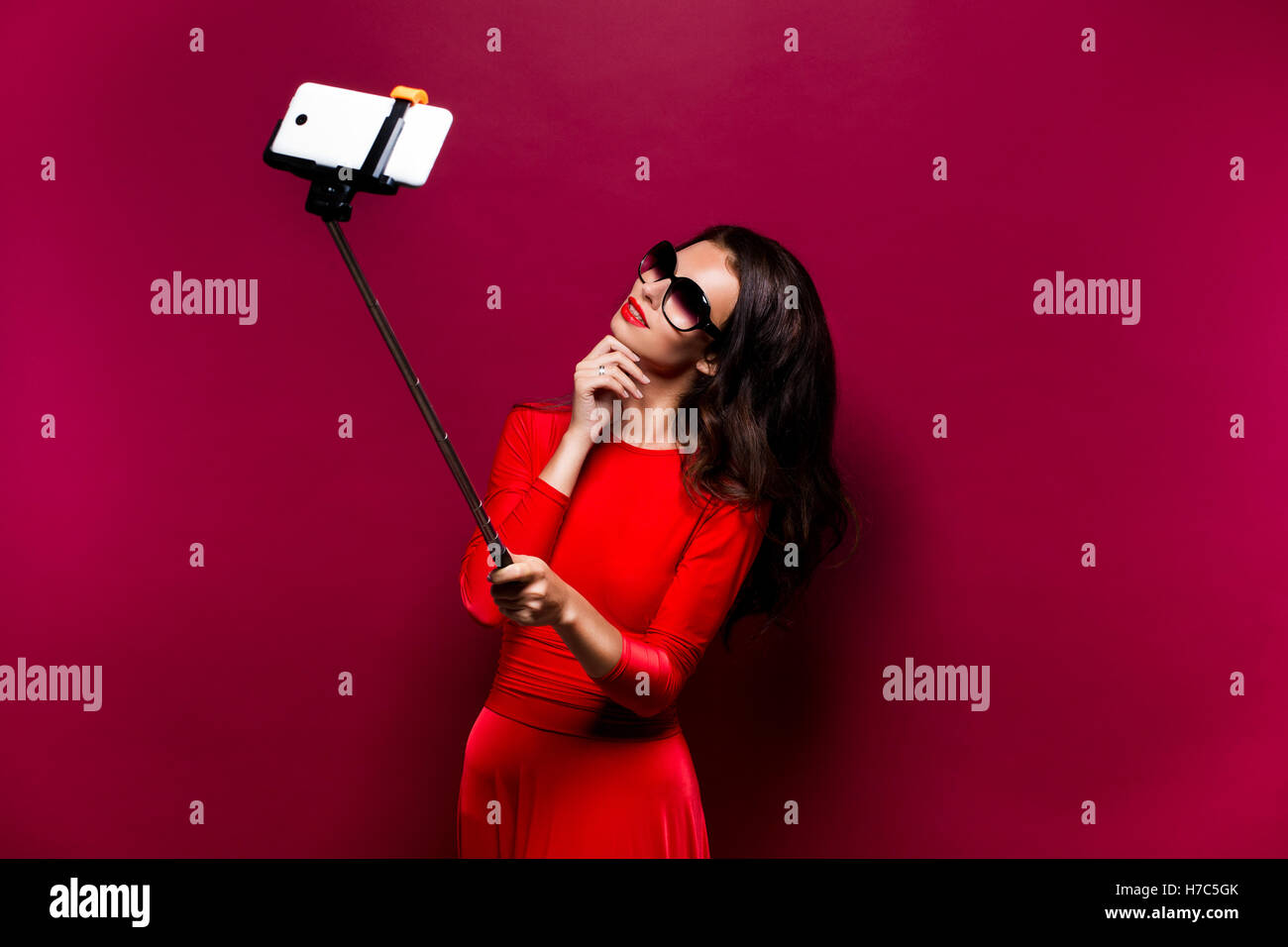 Porträt von schöne Brünette in geiles Kleid und roten Lippen tragen Sonnenbrillen dabei Selfie mit Stick. Isoliert Stockfoto