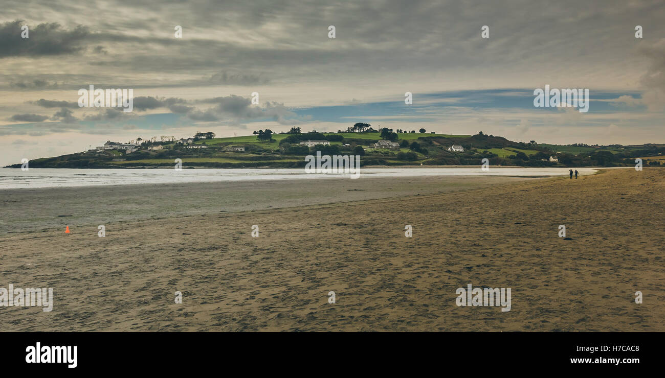 Ein Blick auf einen Felsvorsprung Land ragt zum Meer, vom Strand mit zwei winzigen Silhouetten für Maßstab gesehen. Irland, 2016 Stockfoto