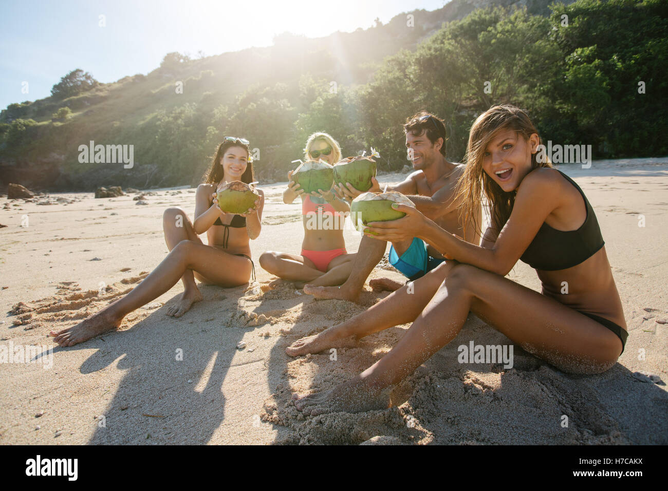 Gruppe junger Freunde Sommerurlaub am Strand mit frischen Kokosnuss Drink zu genießen. Junger Mann und Frauen Toasten mit Kokosnüssen auf Stockfoto
