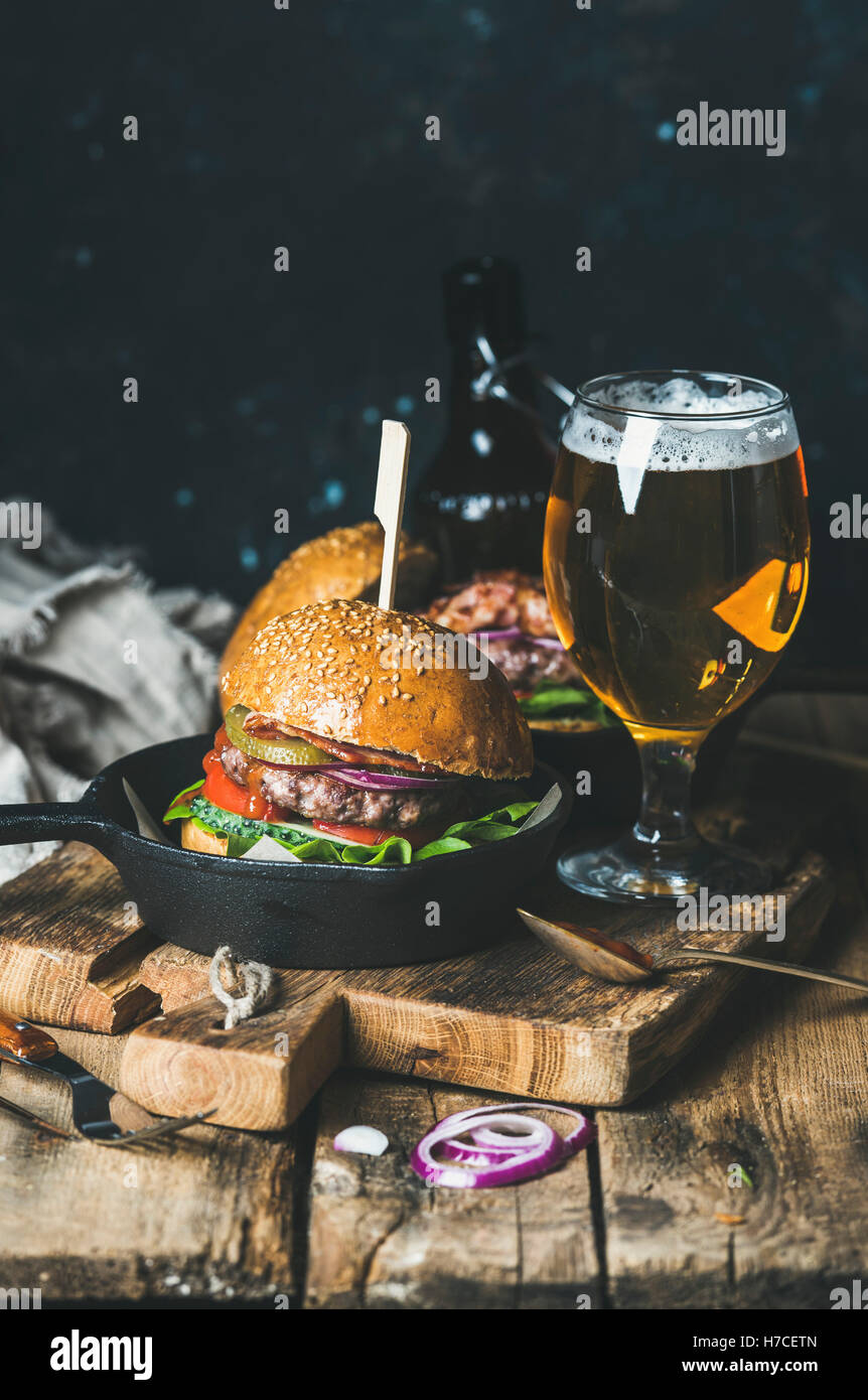 Hausgemachte Rindfleisch-Burger mit knusprigem Speck und Gemüse in kleinen Topf und Glas Weißbier auf rustikalen Portion Brett über schäbige w Stockfoto