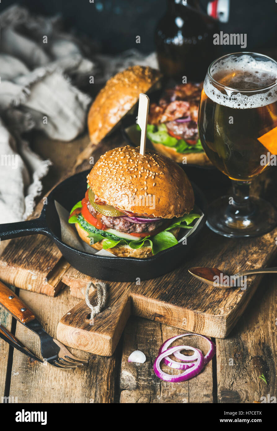 Hausgemachte Rindfleisch-Burger mit knusprigem Speck und Gemüse in kleinen Topf und Glas Weißbier auf rustikalen Portion Brett über schäbig Stockfoto