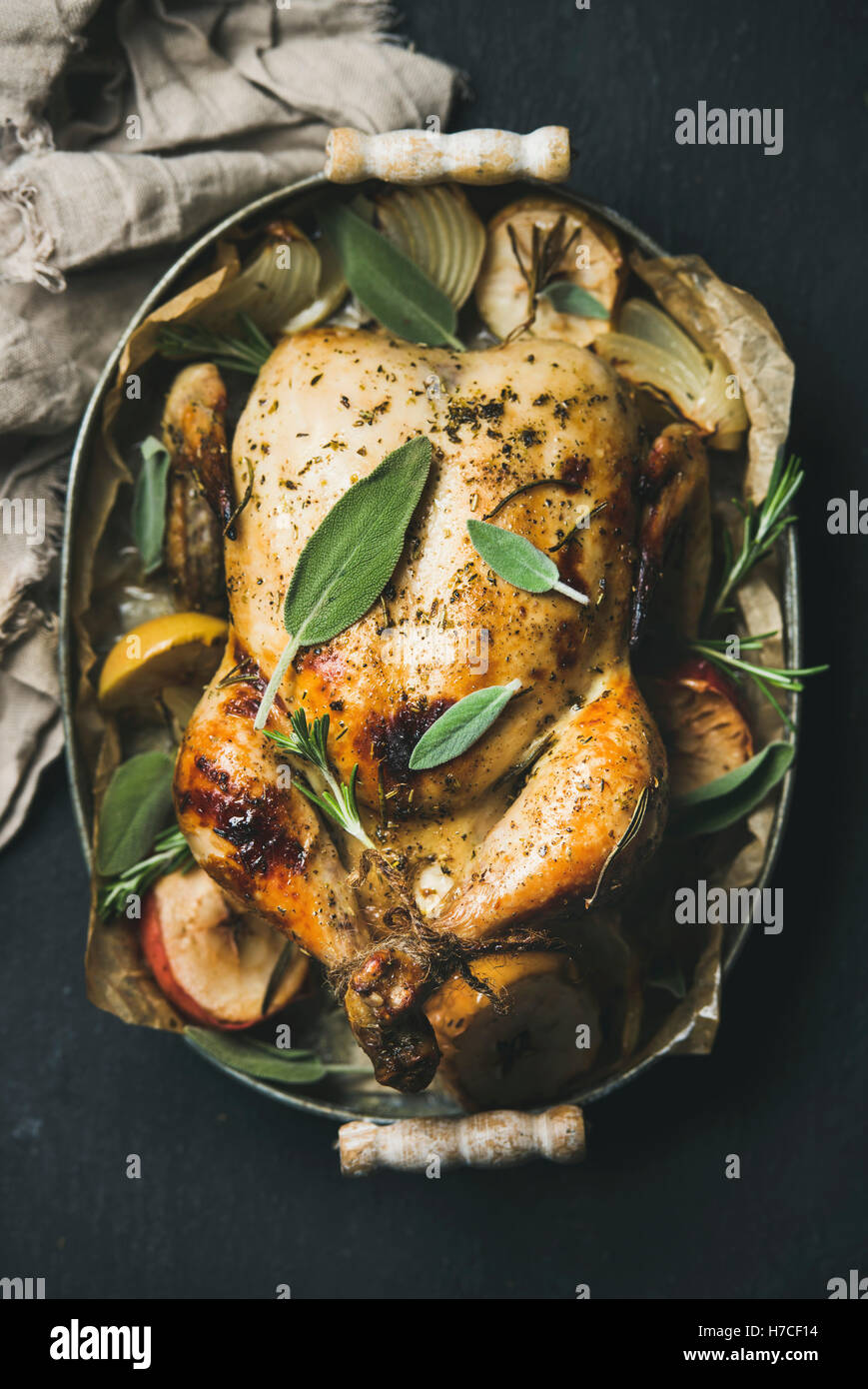 Ofen gebratenes ganzes Huhn mit Zwiebeln, Äpfel und Salbeiblätter in Tablett über dunklem Stein, Draufsicht, selektive fo Stockfoto