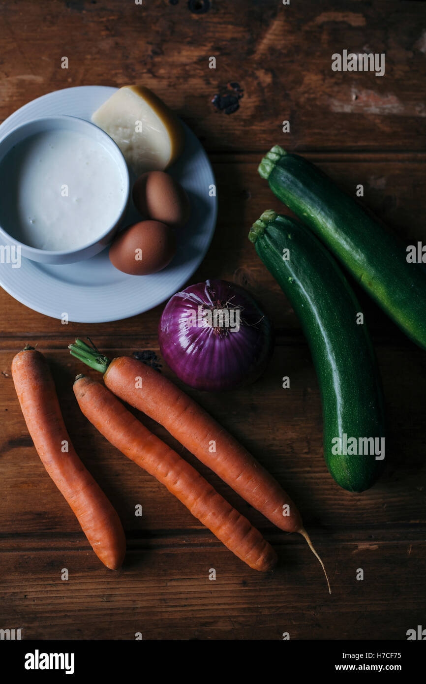 Zucchini, Karotten, rote Zwiebeln, Eiern, Käse und Joghurt auf rustikalen Holztisch Stockfoto