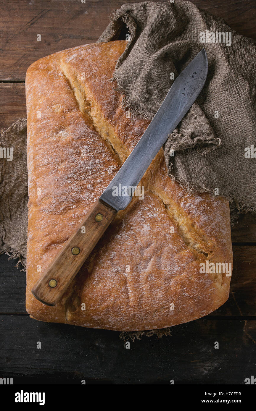 Ganze frisch gebackenes Handwerker Brot unter Sackleinen mit Vintage Messer über alten hölzernen Hintergrund. Draufsicht. Stockfoto