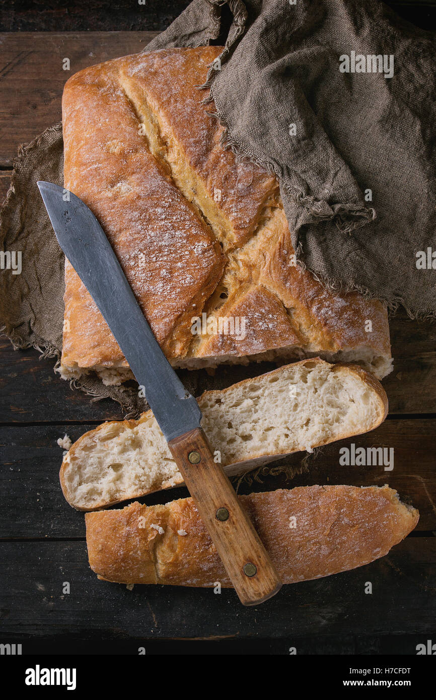 Frische handwerkliche Brot unter Sackleinen mit Vintage Messer über alten hölzernen Hintergrund. Draufsicht. Stockfoto