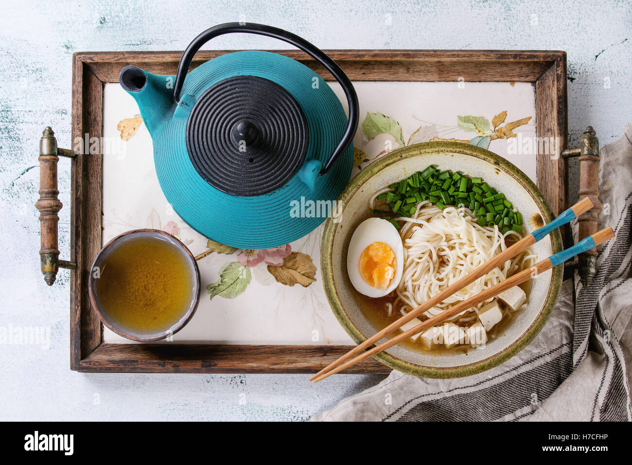 Asiatische Suppe mit Nudeln, Ei, Frühlingszwiebeln und Tofu-Käse, serviert mit Stäbchen, Teekanne und Tasse grüner Tee Stockfoto