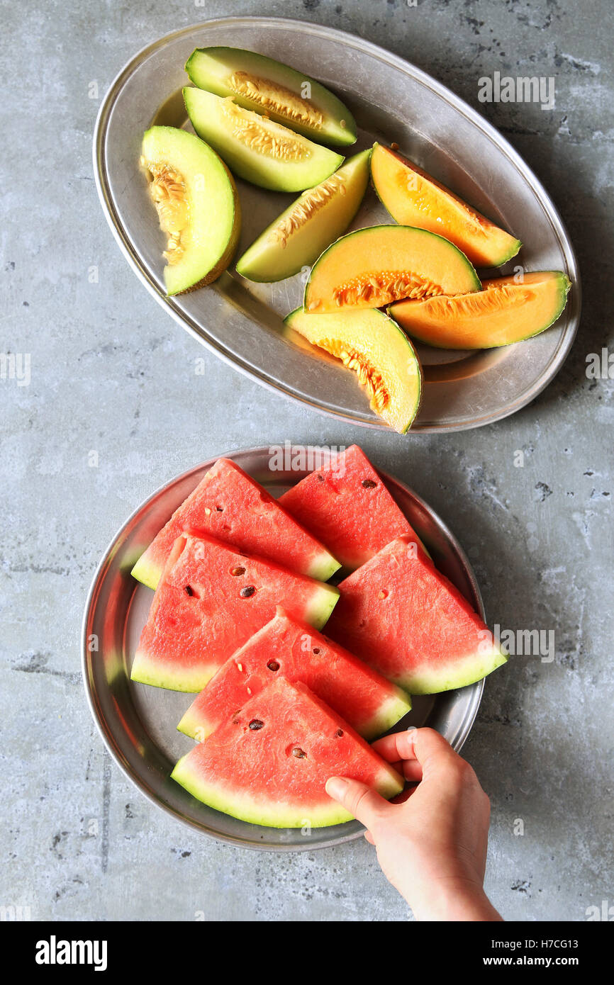 Frisch geschnittenen Melonen auf Tellern anrichten. Weibliche Hände halten ein Stück Wassermelone. Stockfoto