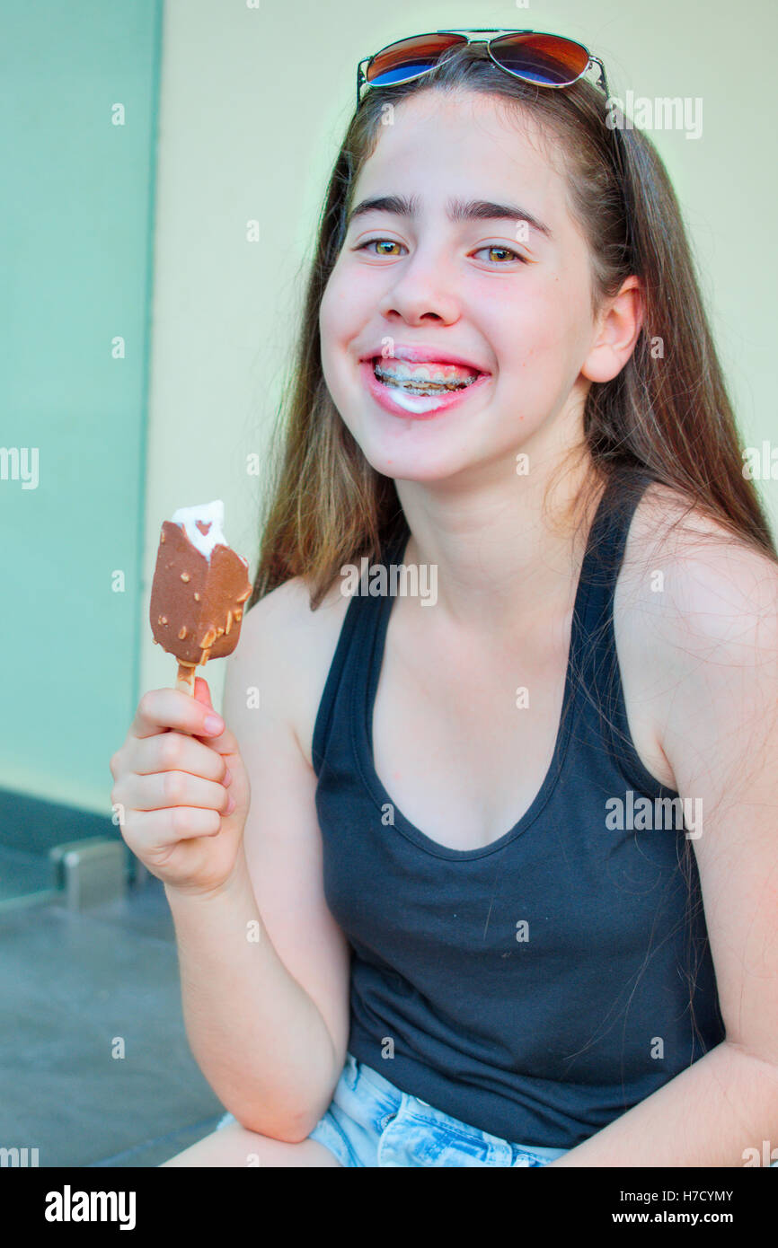 13 Jahre alten Mädchens mit Klammern auf den Zähnen sitzen auf Treppen feiert den Beginn des Sommers durch den Verzehr einer Vanille ic Stockfoto